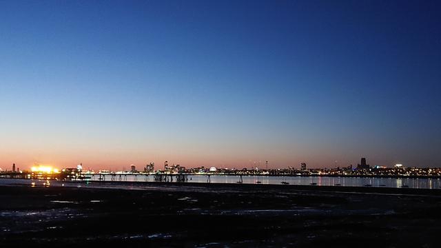 A sunset view across the Mersey from Rock Ferry.  The sky is a beautiful gradient from deep blue above to orangey-red at the horizon and there's a line of the lights of Liverpool running across the scene along the edge of the river.

You can just make out the pier and pipes of the Tranmere oil terminal stretching out into the river, and a row of tiny sailing boats moored along the low water line on this side.