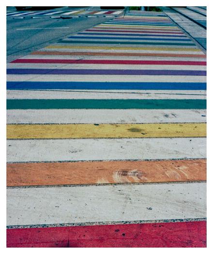 Color photograph of a pedestrian crossing in rainbow colors. The crosswalk is located near the Westbahnhof station in Vienna.