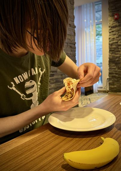 Young man adjusting tortilla before taking bite, bright banana in foreground