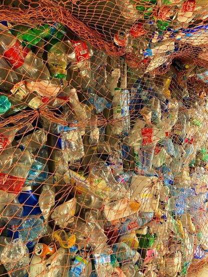 This image shows a collection of various types of plastic bottles that appear to be held together or collected in a mesh or net. The bottles, which include water and soda bottles of different sizes and colors, are likely being gathered for recycling or as part of a waste management process. The diversity of the bottles emphasizes the extent of plastic use and suggests a focus on environmental conservation or recycling efforts.