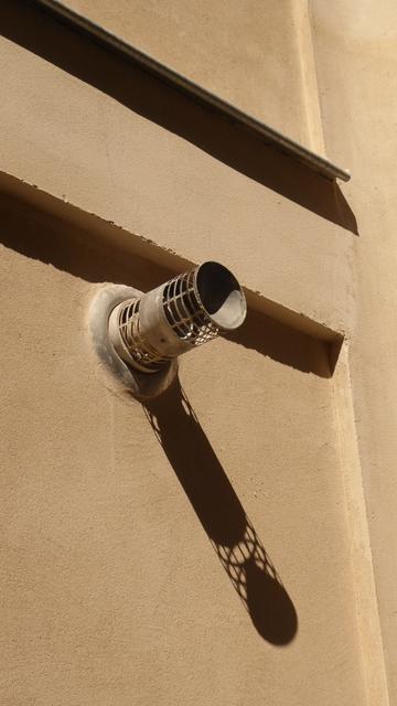 Une bouche de conduite sur un mur couleur sable et son ombre portée.