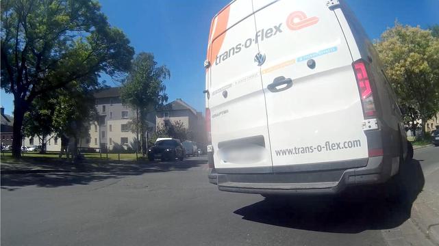 Image of a dashcam on a bicycle just before a junction. The van turns so quickly that the vehicle leans to one side and apparently the steering is so tight that the rear wheels of the van drive over the sidewalk to the right