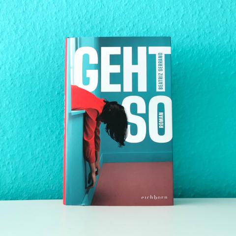 Auf dem Foto ist das Buch "Geht so" von Beatriz Serrano an eine türkise Wand gelehnt auf einer glatten weißen Fläche fotografiert.