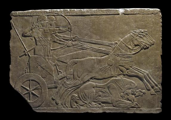 well-lit photo of a shallow relief of a chariot galloping from left to right. The driver holds the reins, the archer draws a bow, and a lion has fallen to the ground with three arrows in its body