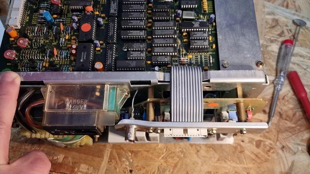 Ansicht eines geöffneten Hameg HM205-3 Oszilloskop von hinten, zu sehen ist ein verbogenes Blech mit BNC-Buchse, einige IC und Flachbandkabel