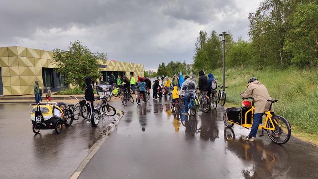 Eine Gruppe Radfahrer:innen wartet am Informationszentrum Kienberg in Marzahn-Hellersdorf bei der Startkundgebung der Kidical Mass. Man sieht ca. 25-30 Personen, darunter Kinder.