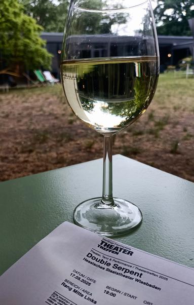 Auf einem kleinen Tisch im Garten das Ticket und ein glas Weißwein.