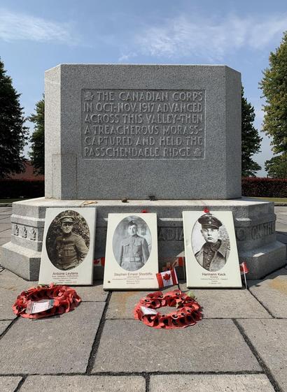 This image shows a war memorial dedicated to the Canadian Corps, indicating their military effort in October and November 1917 during World War I. The inscription on the monument marks their advancement across a valley, describing it as a treacherous morass, and their capture and holding of Passchendaele Ridge.

In front of the monument, there are three portraits placed on the base, each with a name beneath them: Antoine Leytens, Stephen Ernest Shortliffe, and Hermann Keck. These likely represent soldiers who participated in the historical events commemorated by the memorial. Below the portraits, there are wreaths adorned with red poppies, a symbol often used to remember those who have died in military service, particularly in British and Commonwealth countries. Small Canadian flags are also placed near the portraits, emphasizing the memorial’s connection to Canada and its historical military contributions.