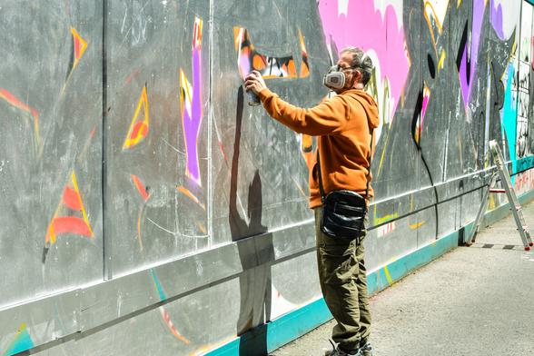 Muralist with protective mask, spray-painting a wall