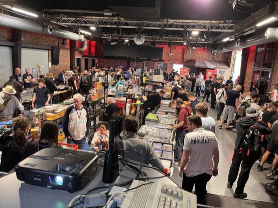 Foto von einer Halle. Überall stehen Verkaufstische mit Games und Zubehör