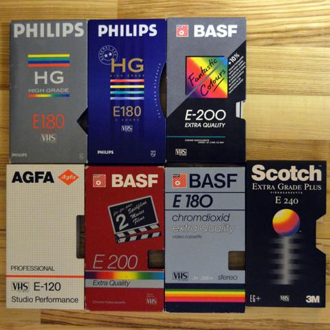 Assorted covers of recordable VHS tapes from Philips, BASF, Agfa and Scotch, without the VHS cassettes themselves, on a wooden floor.