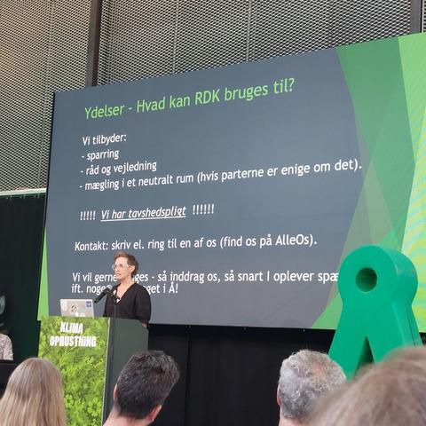 Trine Aslaug Hansen holder tale for Rådet for Dialog og Konflikthåndtering (RDK).

Baggrundsskærmen er mørkegrå med Grønne striber i siderne.

Der står: 
Overskrift med grøn tekst: Ydelser - Hvad kan RDK bruges til?

Vi tilbyder:
- Sparring
- Råd og vejledning 
- Mægling i et privat rum (hvis parterne er enige om det).

!!!!! Vi har tavshedspligt !!!!!

Kontakt: Skriv el. ring til en af os (find os på AlleOS).

Vi vil gerne inddrages - så indrag os, så snart i oplever spændinger ift. nogen eller noget i Alternativet!

(AlleOS er Alternativet's medlemsportal)