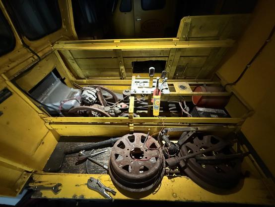 The inside of a yellow wooden vehicle with a small engine inside, and a control panel with several levers sticking up in the middle. Tools and equipment are scattered around