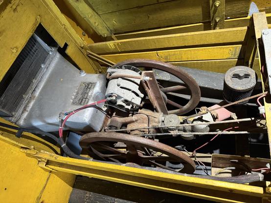 A small engine with flywheels on either side, a generator on top, and a cooling system sticking through the front of the yellow wooden vehicle