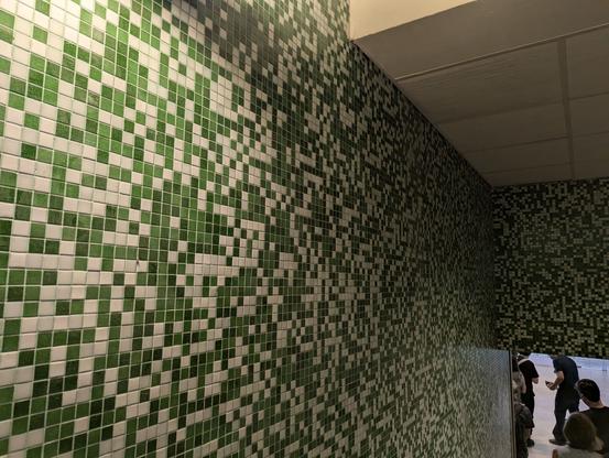 The wall of one of the stairwells of Lisbon airport, the wall has tiles on it that look like the green &#34;commits per day&#34; tiles you would see on github, with various shades of green and white