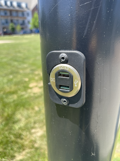 A close up of a USB charging port, outside, on a light pole.