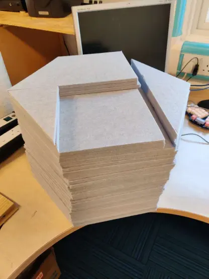 A big hexagon shaped stack of acoustic felt tiles. There are 18 full hexagons, 18 half-hegagons and a few other hexagon parts