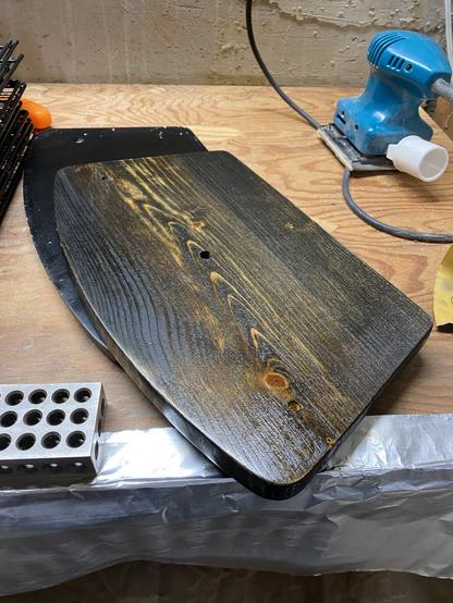 top of a cd storage tower base, black stained with three layers of shellac, on a workbench. the harder parts of the wood take up less black stain so with the varnish show up as yellow-gold stripes in a woodgrain pattern