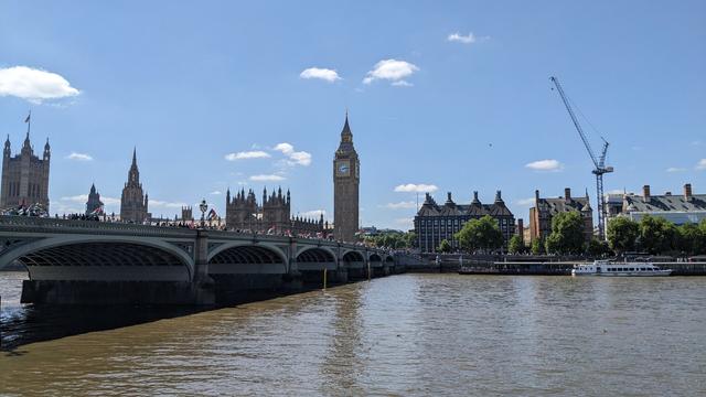 A view over the River Thames in London, showing Westminster Bridge with the Houses of Parliament behind it. A large protest march fills the bridge and Victoria Embankment, with many Palestinian flags being waved.