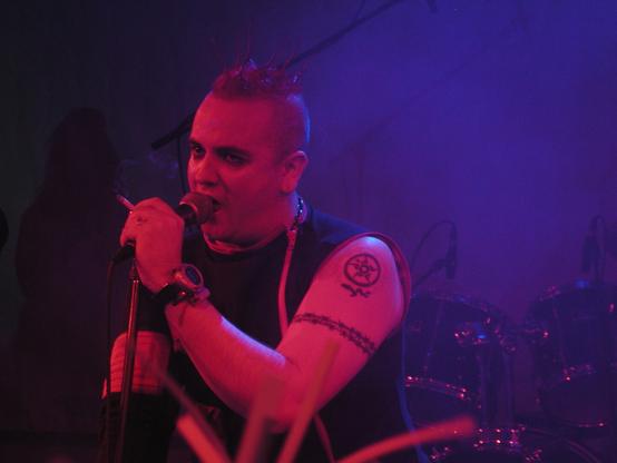 Frontman of a goth band performing under red lights at a festival, many years ago.