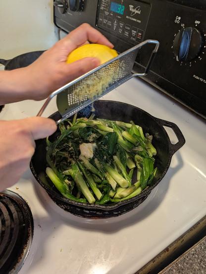 Lemon being zested into a pan of ramps and hostas