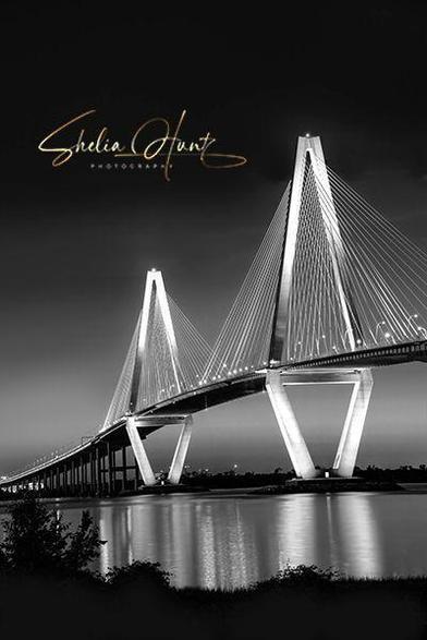 Stunning black and white image of the Arthur J. Ravenel Bridge at Charleston, South Carolina. Photo was taken just after sunset when the bridge was fully illuminated and cast a beautiful glow on the Cooper River. Image is vertical (portrait mode). Photo by Shelia Hunt Photography.
