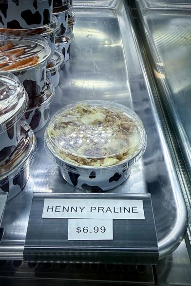 A photo of a small to-go cheesecake behind a sign that reads HENNY PRALINE