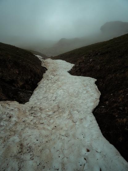Snowfield in the Swiss Alps. Clouds obscure the peaks in the background. Landscape photography by Marco Zedler.
