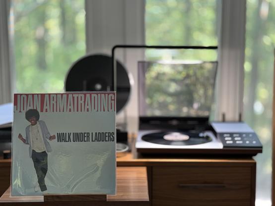 Joan Armatrading - Walk Under Ladders LP cover.

Joan, on a white background, looking pretty carefree. Name above in white on a red background. Title to the right in black.

The black LP plays on a vintage, restored Bang & Olufsen Beogram 8002 linear-tracking turntable to the right.