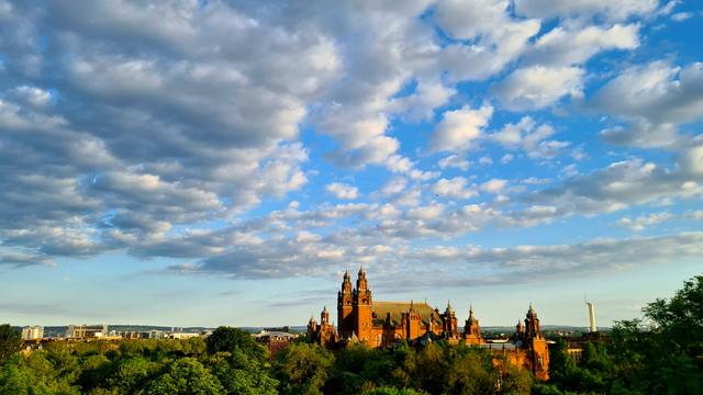 A late evening view across a Glasgow park witb a large and ornate 1901 red sandstone art gallery dominating the skyline.