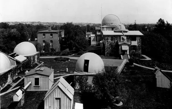 The image depicts a historical observatory complex with several domed structures, likely used for astronomical observations. There are also smaller buildings and a landscaped area, suggesting a well-maintained facility. The setting appears to be outdoors, with trees and structures in the background.

Image Credits: Wikimedia / Harvard College Observatory / Public domain