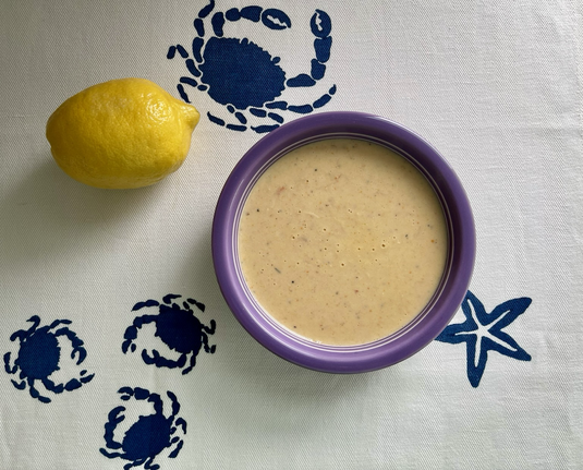 In a center is a purple bowl with sea crab soup. In the upper corner to the left is an uncut lemon. The tablecloth has crabs and star.