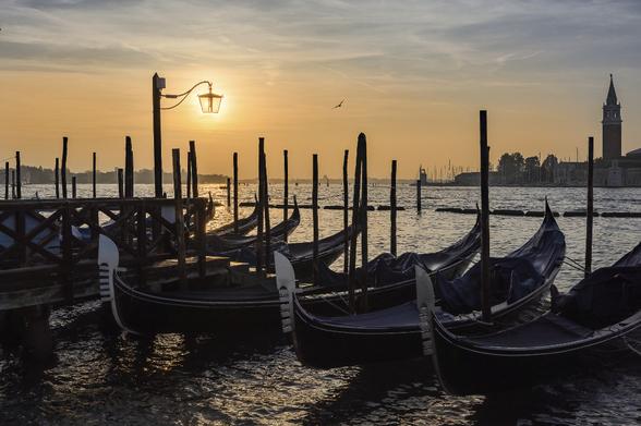Sunrise on Venetian lagoon with docked gondola in the foreground. The orange glowing sun appears through a lamp post.