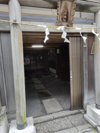 A photo of a small urbana Shinto shrine . You see paper charms strung over a low doorway