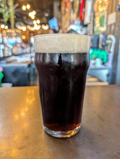 A dark beer in a glass with a healthy amount of foam head, sitting on a bar