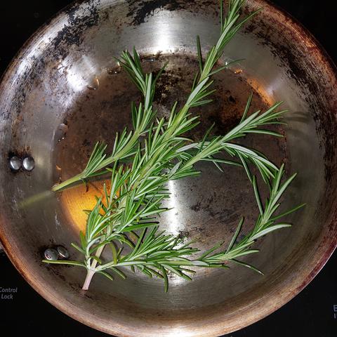A small skillet with several branches of fresh rosemary inside.