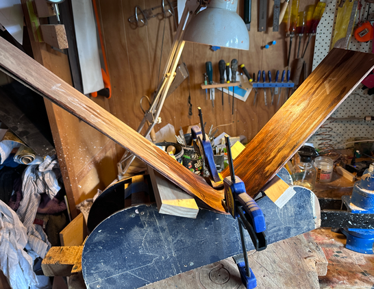 a messy workbench with some bent wood that will ultimately become the sides of a guitar - there's a single near-90 degree bend in two thin slats of wood.