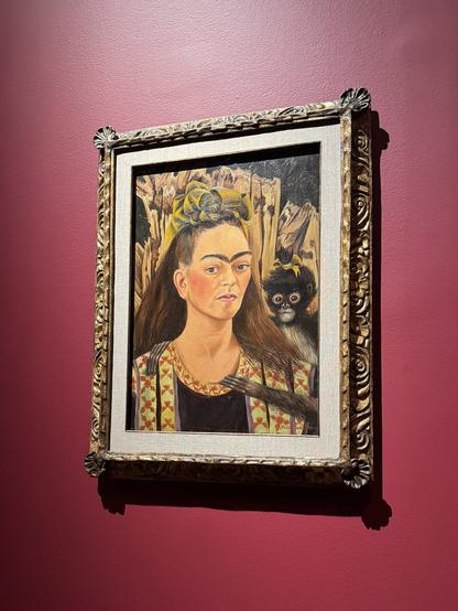 The image features a framed painting displayed on a maroon wall. The painting depicts a woman with a distinctive hairstyle, characterized by a thick, dark eyebrow and a yellow headband. She wears a colorful garment with a patterned design, featuring red and yellow elements. A small monkey with a yellow bow is positioned behind her, adding a playful element to the composition. The background consists of abstract, earthy tones, possibly representing natural elements. The frame is ornate, with intricate carvings and a golden hue, enhancing the overall aesthetic of the artwork.

Provided by @altbot@fuzzies.wtf, generated privately and locally using Ovis2-8B

🌱 Energy used: 0.151 Wh