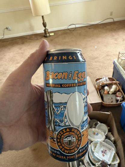 A can of beer with bacon and eggs holding hands near the seashore. The color scheme is sea blue, white and orange.