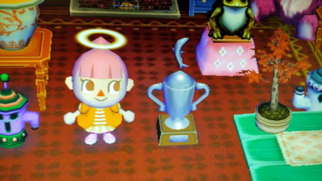 The player standing in her house next to a large silver cup style trophy with a fish on top