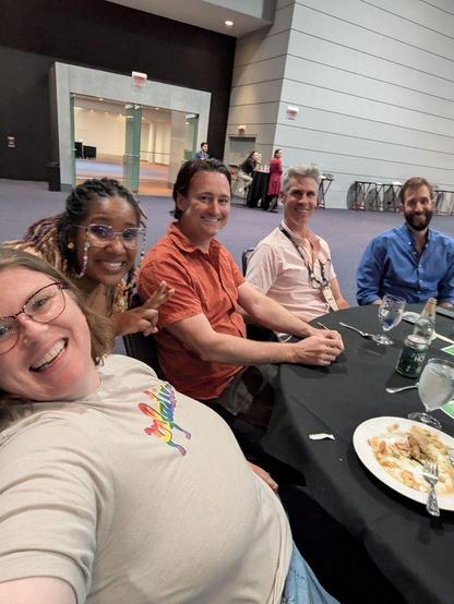 A selfie of the author with four smiling friends sitting at a round, black dinner table.