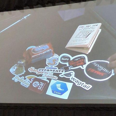 A random pile of loot that includes the auctioneer's pen, a chocolate bar, several stickers from various tech events, and a Wagtail enamel pin.