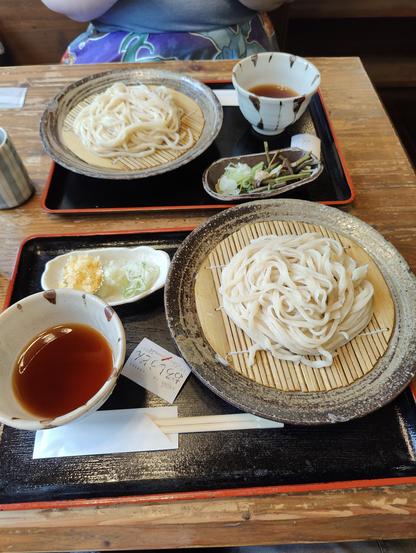A photo of two trays of noodles with dipping sauces Ave garnishes