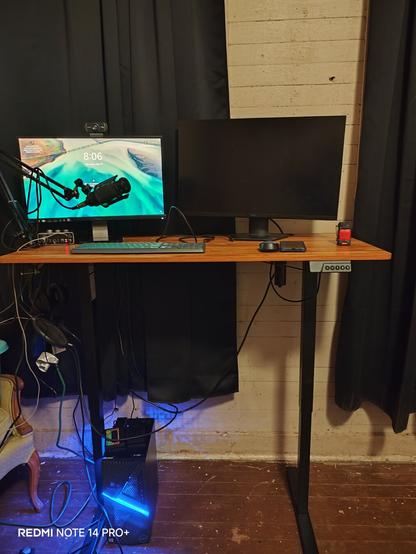 2 monitors, a standing desk on stand mode. A Dell computer on the bottom. Two black curtains. White wall and wooden floor.