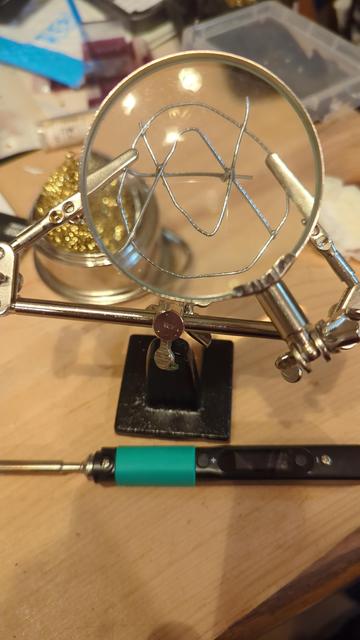 Paperclip emblem art displayed through a magnifying lens, on some helping hands with a soldering iron laying in front.