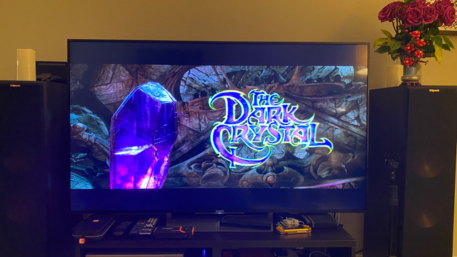 Wide shot of my bigass 65" Sony Bravia TV and two Kilpsch floor speakers, with the TV displaying the title screen to the film "The Dark Crystal"