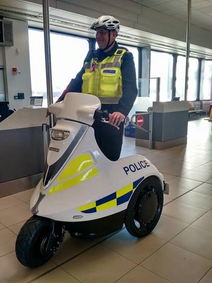 A policeman with a cycle helmet stands on a white scooter thing
