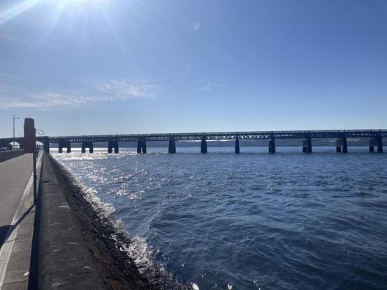 View of Tay firth along the flood wall and pedestrian walkway with the sun risen over the rail bridge on a bright clear day. The wind is up so the water splashes against the wall