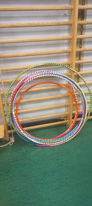 Ein paar bunte Hula Hoops stehen angelehnt an eine Kletterwand in einer Turnhalle und warten darauf gespielt zu werden.
