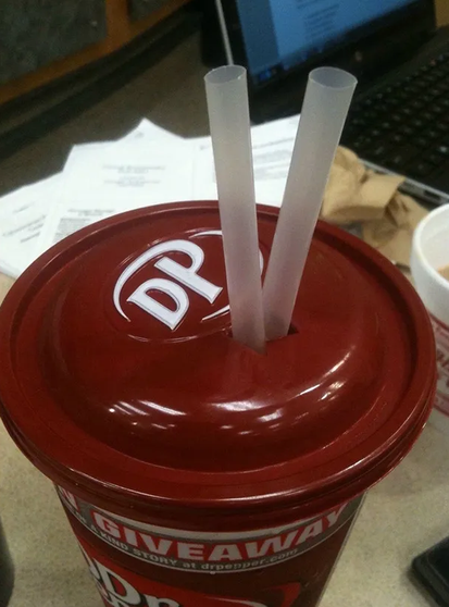 A cup with a lid on it, there lid has the letter DP written on it, there are 2 straws inserted into the lid and cup.
